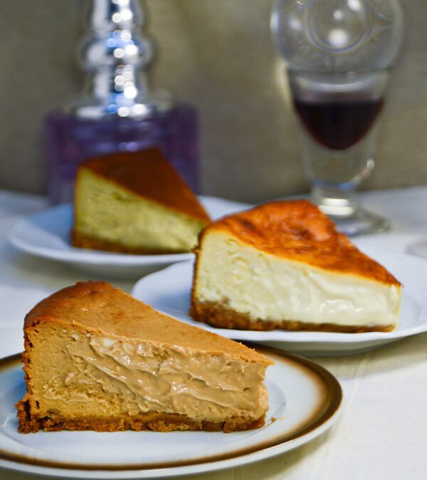 Imagen de tres porciones de tarta de queso de tres sabores distintos: dulce de leche, clásica y de pistacho. Las tartas son tostadas por arriba y extremadamente cremosas por dentro, con base de galleta crocante.