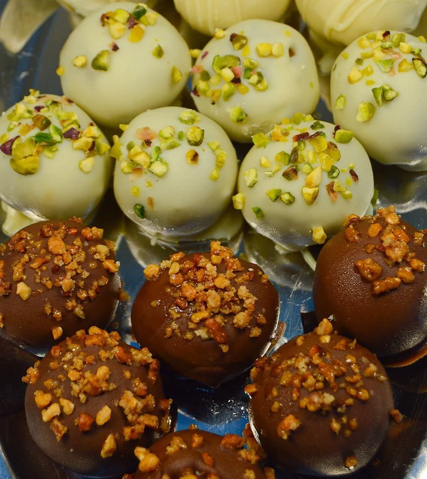 Imagen de los delis de varios sabores, que son bolitas de un solo bocado de masa de bizcocho con distintos sabores, cubiertos con chocolate y decorados.